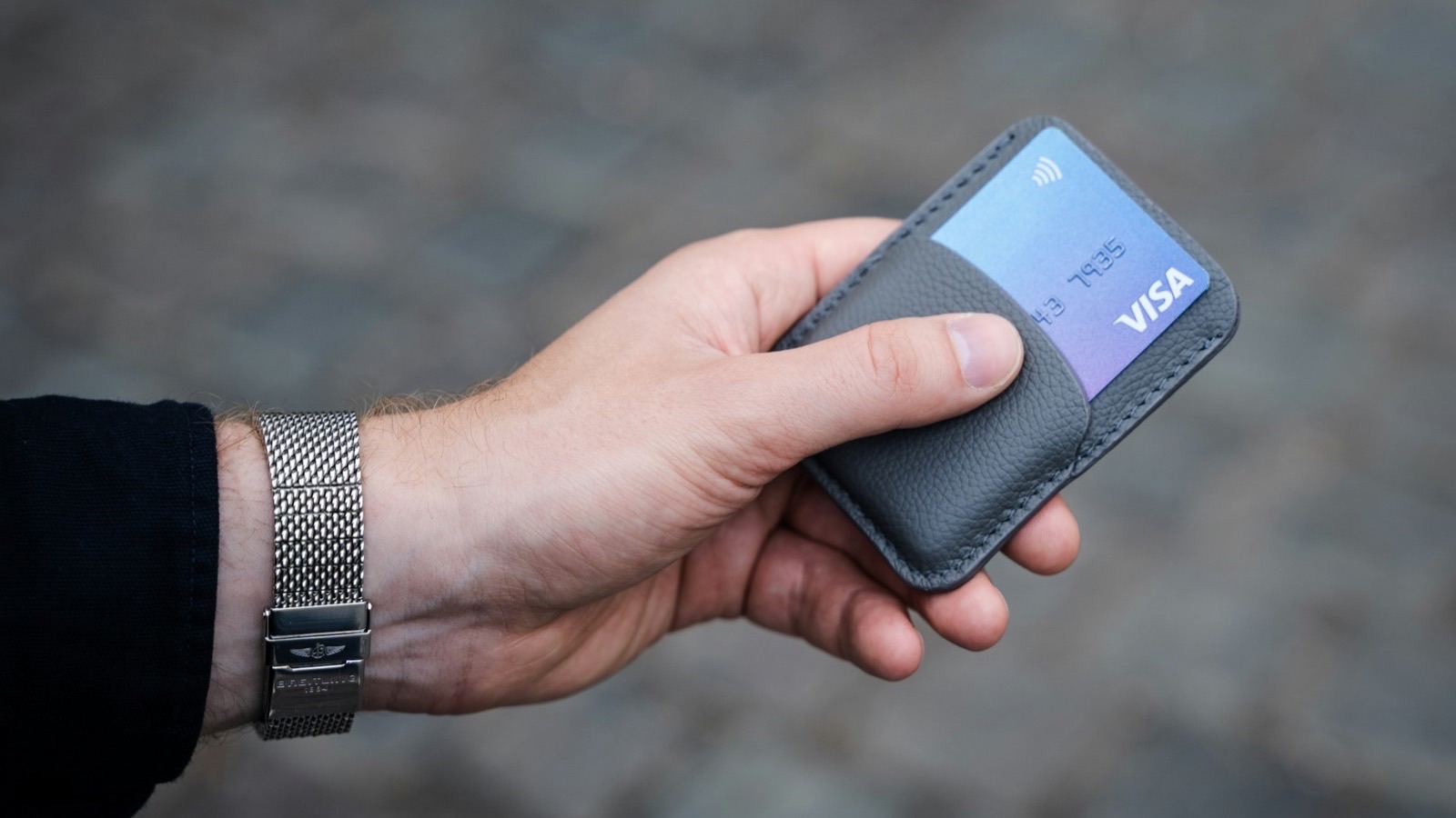 Mão segurando um porta-cartões de couro cinza com um cartão de bandeira Visa