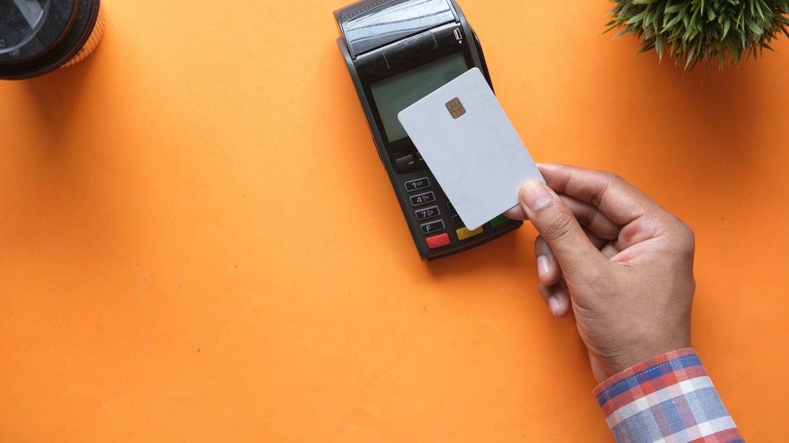 Mão aproximando um cartão branco com chip de uma maquininha de pagamento sobre fundo laranja