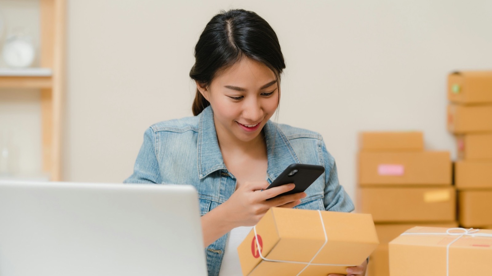 Lojista registra pelo celular o envio de um pacote, ao lado de caixas prontas para entrega