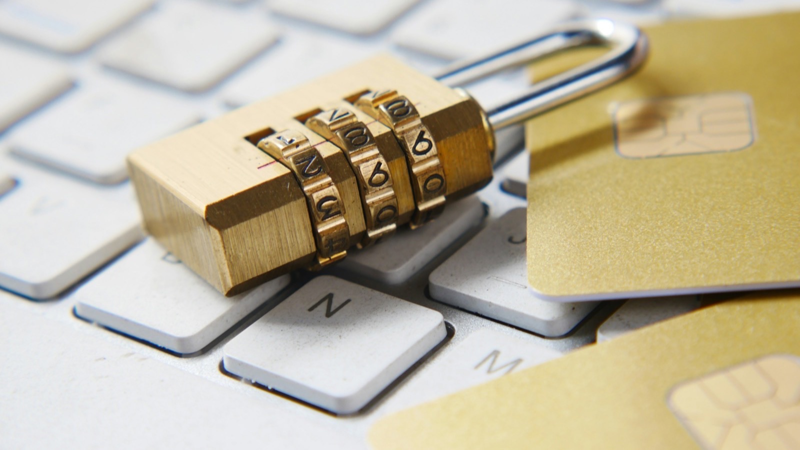Cadeado de segredo dourado sobre um teclado, ao lado de cartões com chip