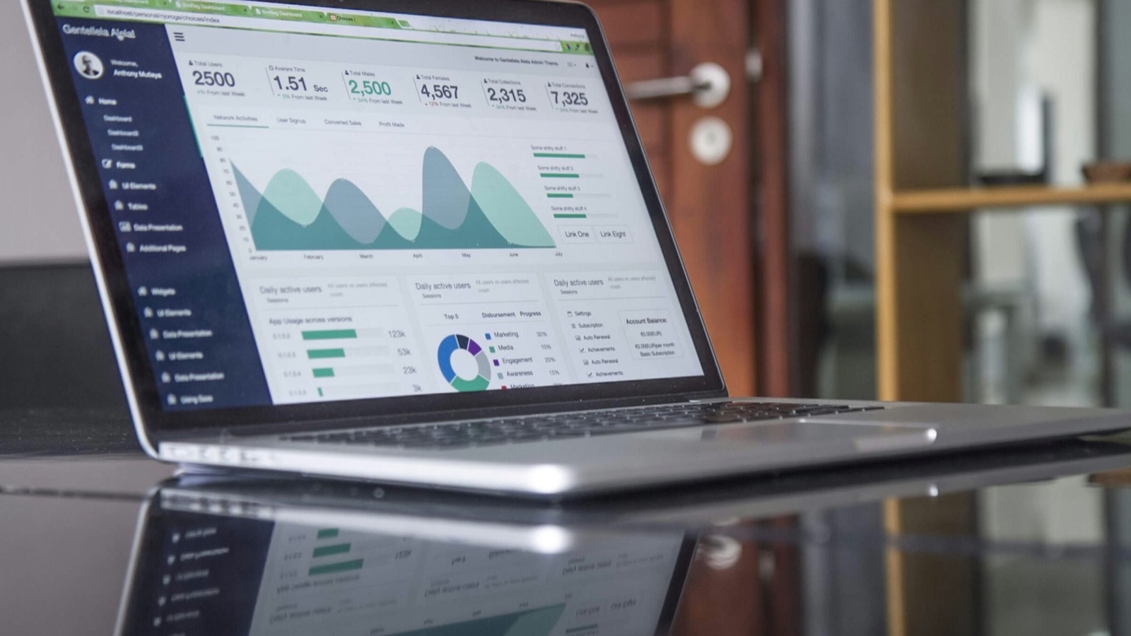 Notebook aberto sobre mesa de vidro mostrando um painel com gráficos e indicadores financeiros
