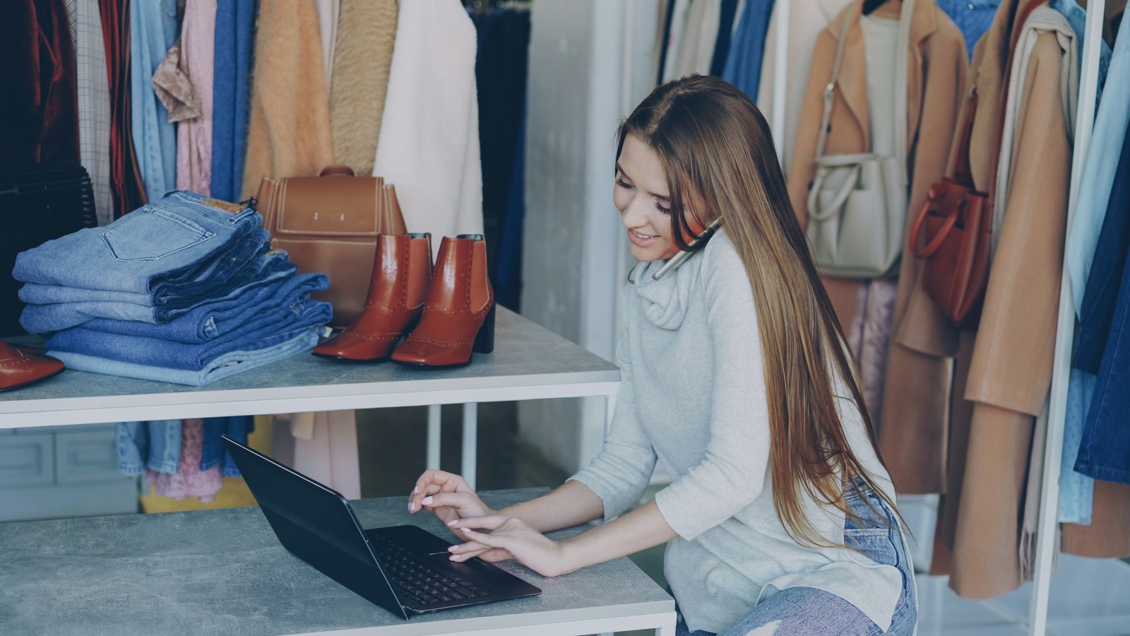 Lojista de roupas trabalhando no notebook em meio às araras da loja